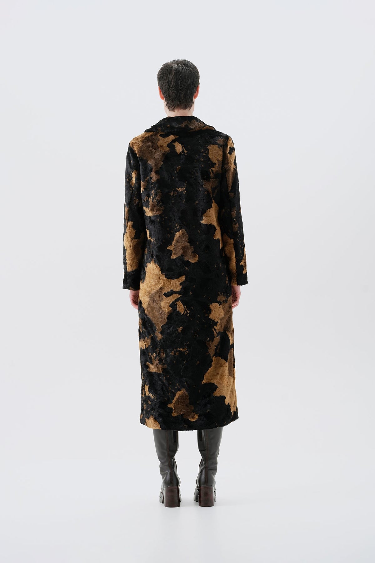Model pictured from the back wearing a long black and brown faux fur coat with a cow pattern on a white background
