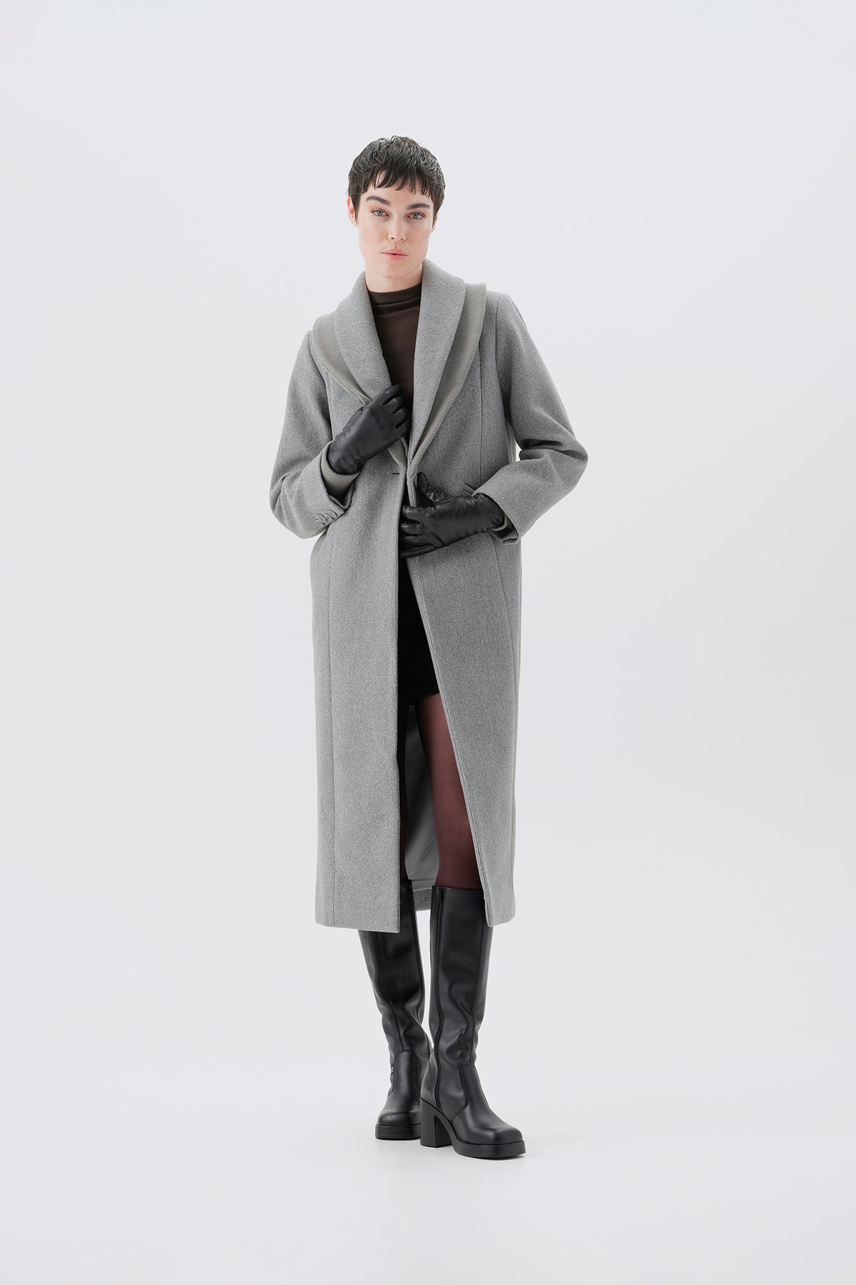 Model wearing a gray long coat and black boots on a white background