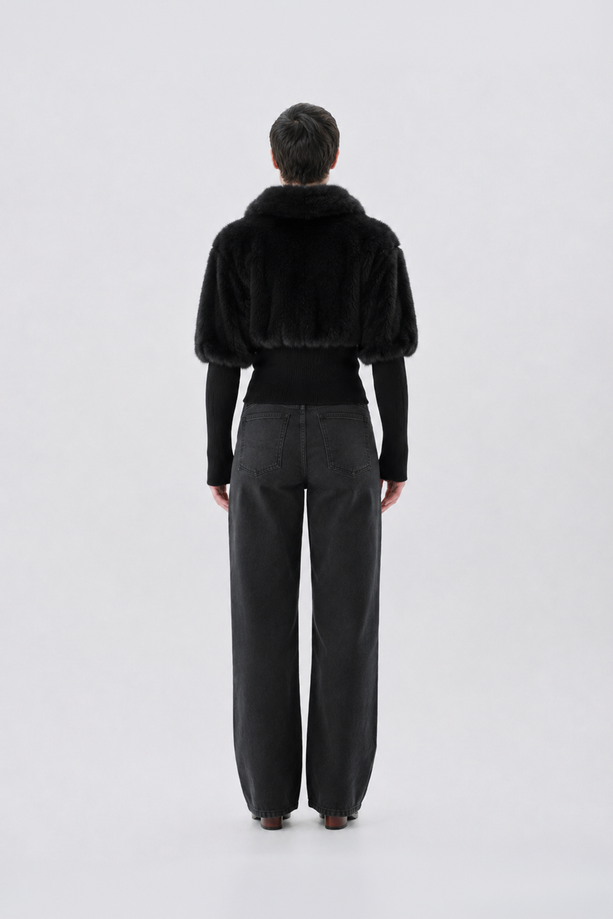 A model viewed from the back wearing a black faux-fur jacket.