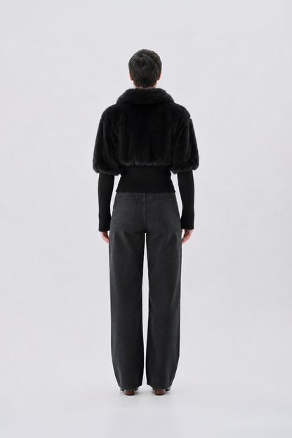 A model viewed from the back wearing a black faux-fur jacket.