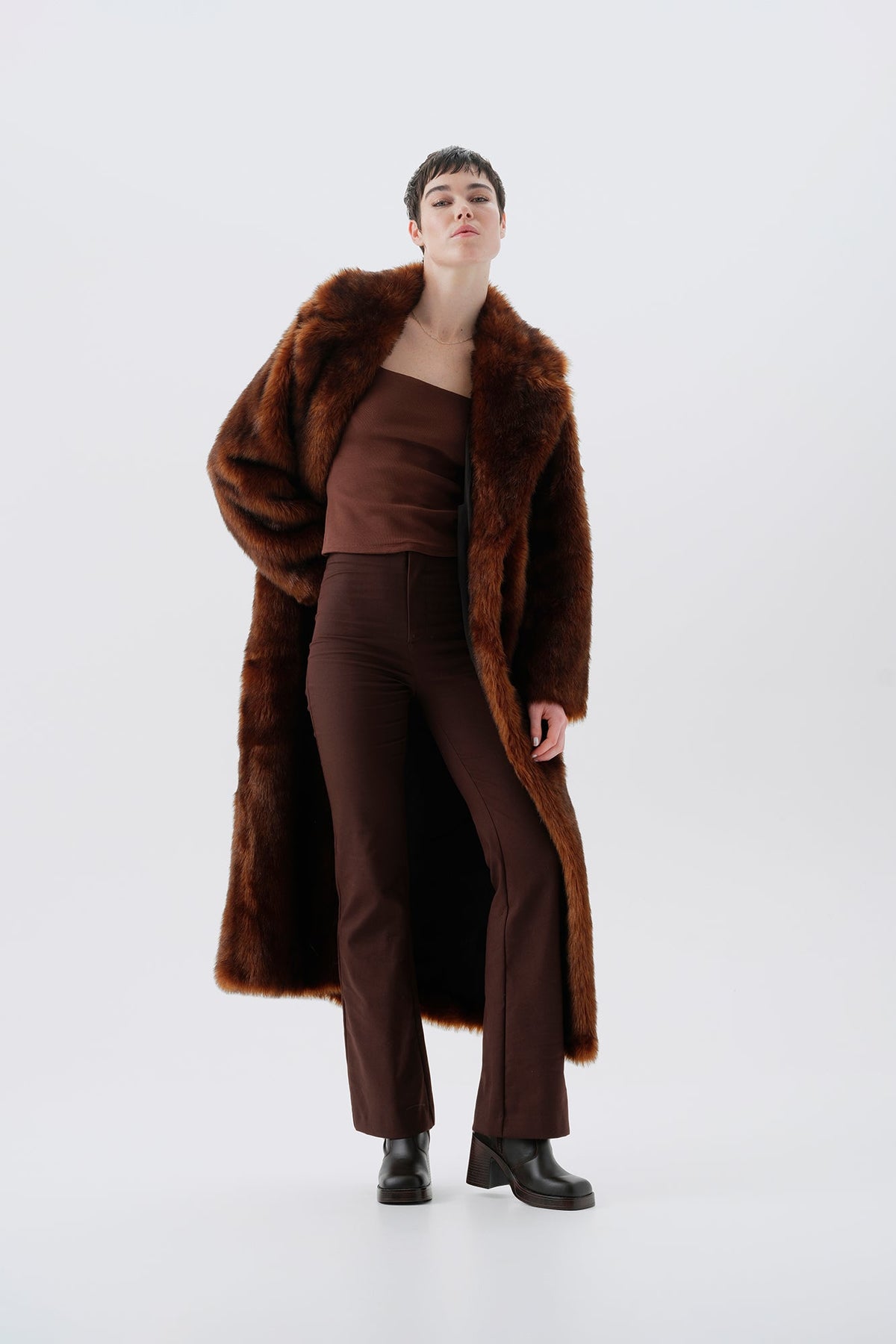 Model wearing a warm and long brown faux fur coat on a white background