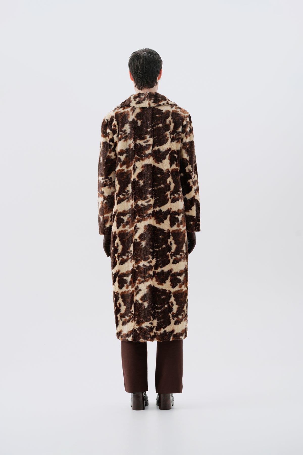Model wearing a faux fur cow print long coat on a white background