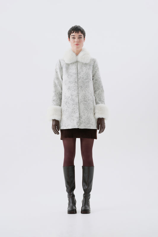 A model viewed from the front wearing a patterned white and grey faux-fur coat with white faux-fur collar and cuffs.