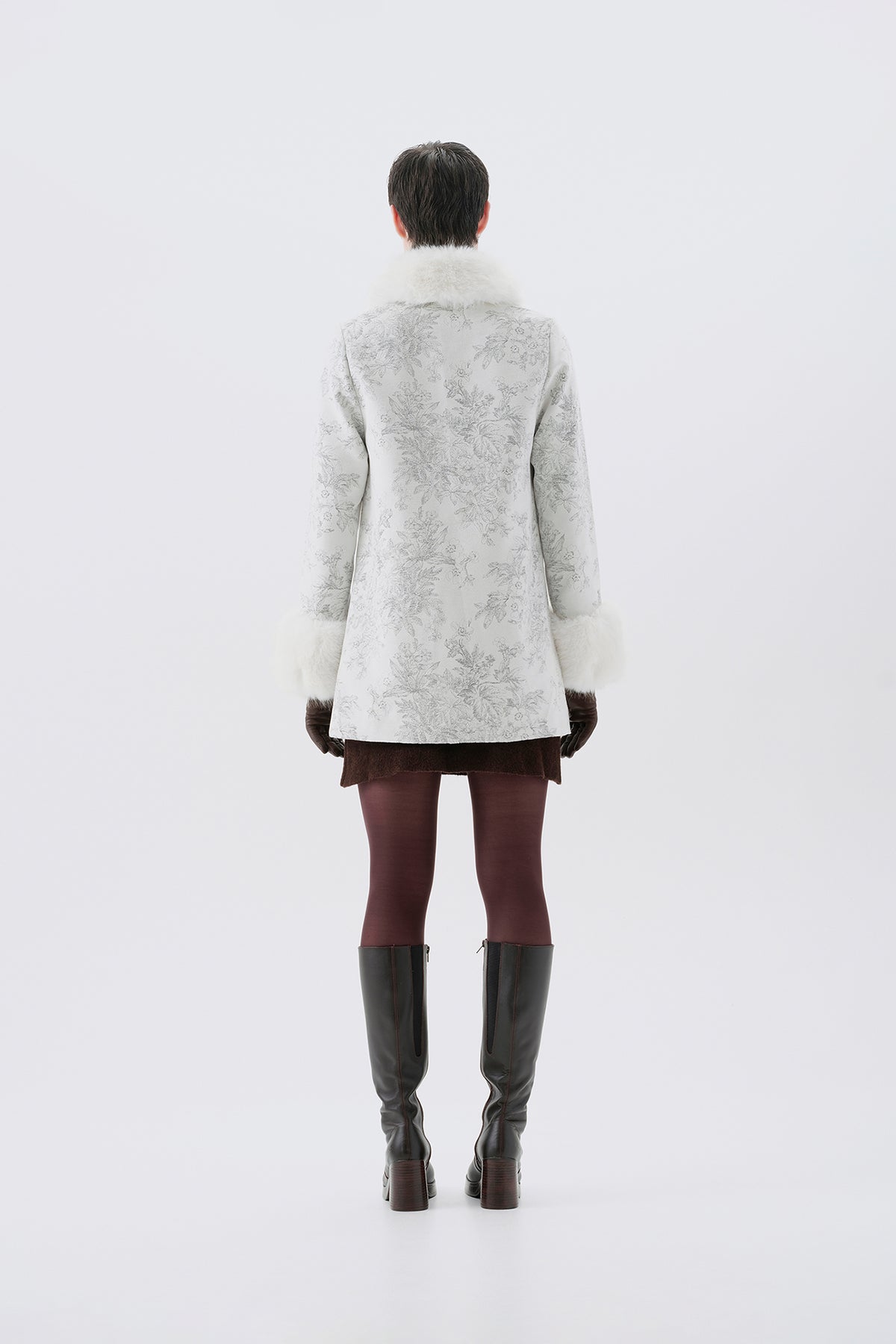 A model viewed from the back wearing a patterned white and grey faux-fur coat with white faux-fur collar and cuffs.