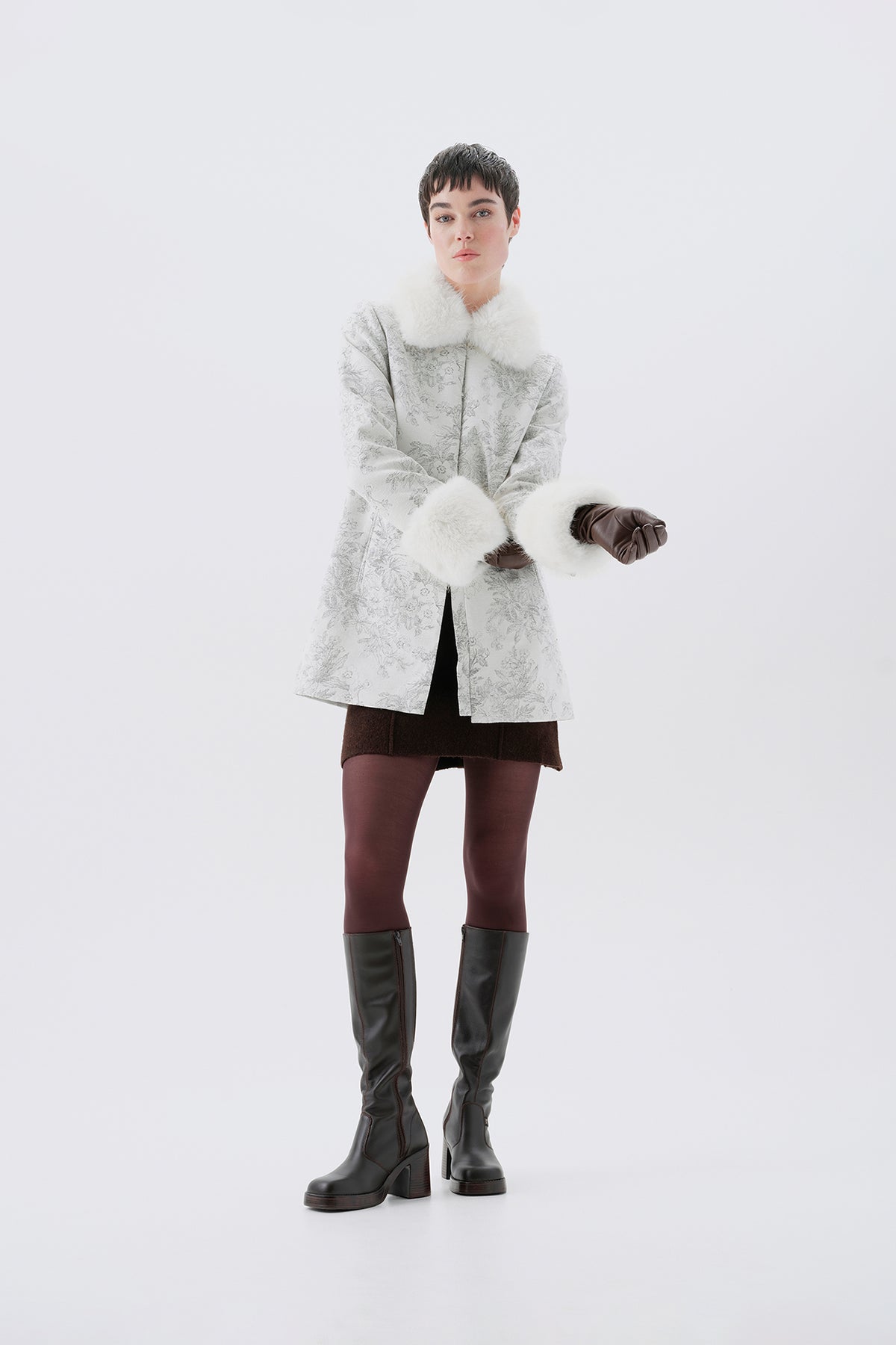 A model in a three-quarter view wearing a patterned white and grey faux-fur coat with white faux-fur collar and cuffs.