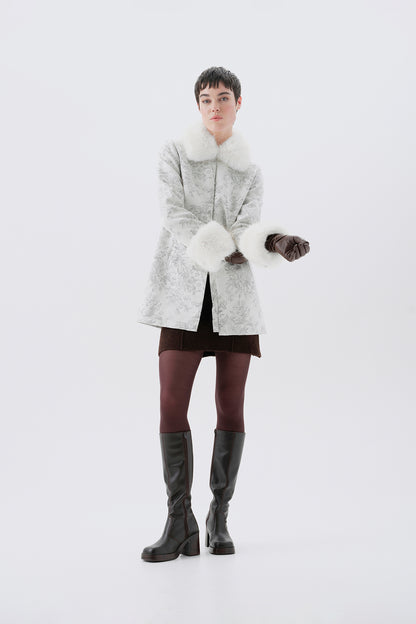 A model in a three-quarter view wearing a patterned white and grey faux-fur coat with white faux-fur collar and cuffs.